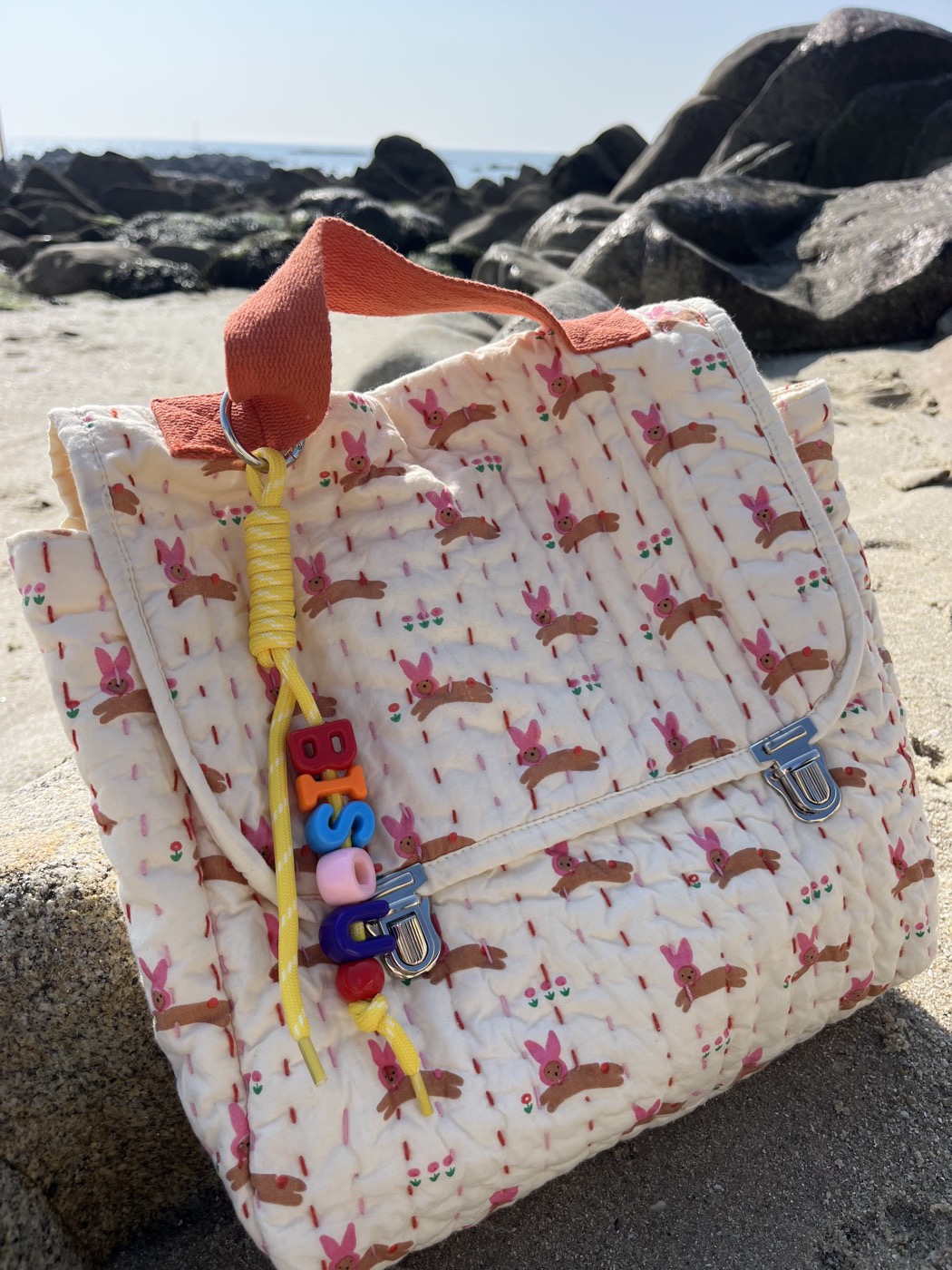 Grigris BISOU jaune accroché à un sac sur la plage